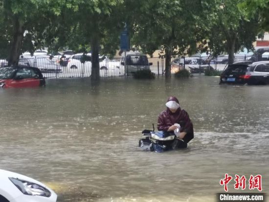 　图为郑州市民众推着电动车涉水出行。　刘鹏 摄
