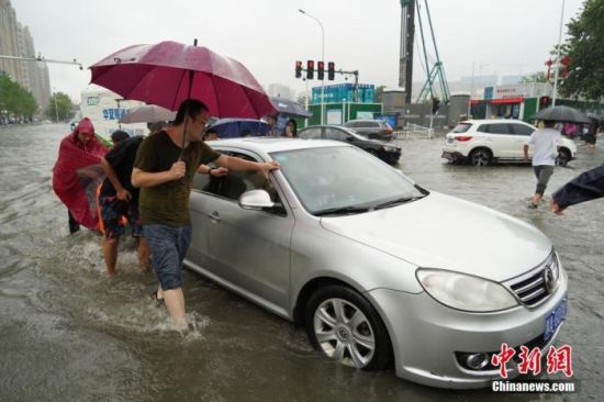 7月20日，河南郑州，一车辆经过积水路段后抛锚，众人帮忙将其推出。近日，郑州连遭暴雨袭击，持续强降雨导致部分街道积水严重。 中新社记者 李超庆 摄