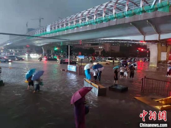 图为7月20日晚间，市民在雨中趟水前行。　阚力 摄