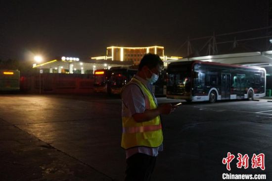 　夜幕中林贺站在场站入口为结束运营的公交车安排充电位置。　韩章云 摄